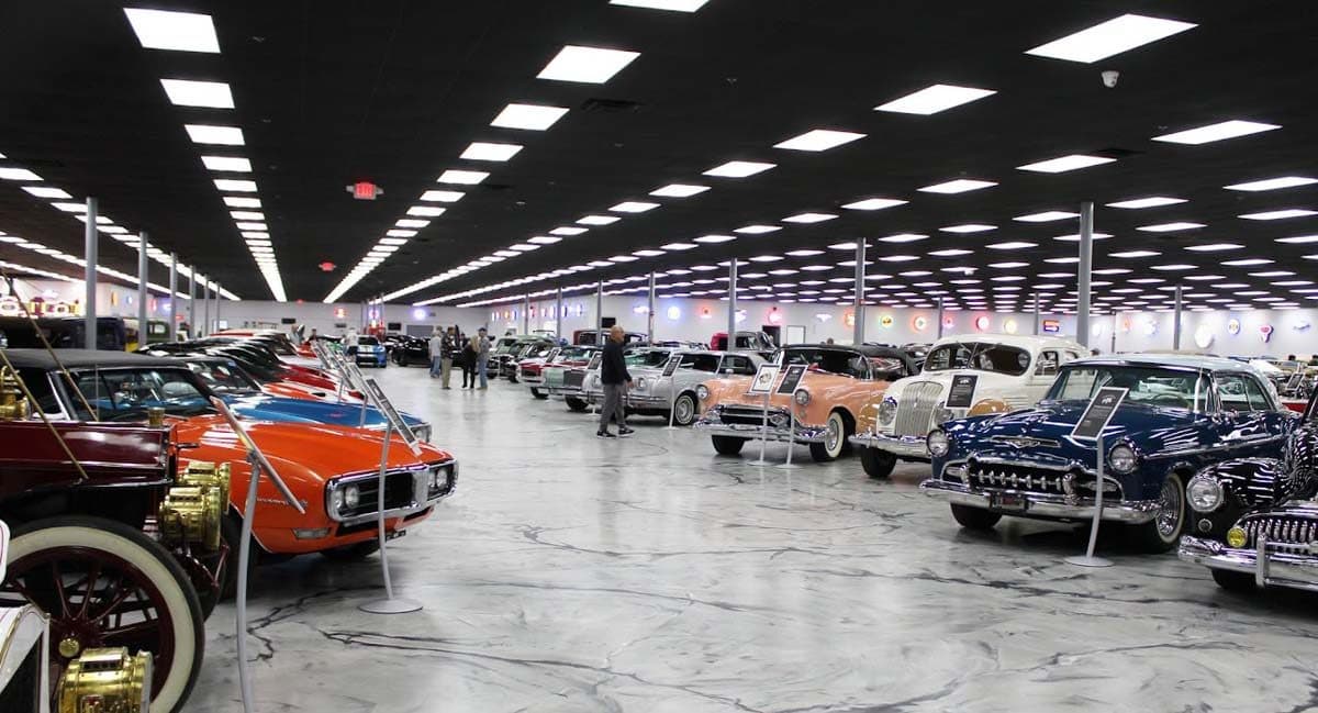 The museum's main hall: two long rows of collector cars under the gallery lights, receding toward the neon wall at the far end.