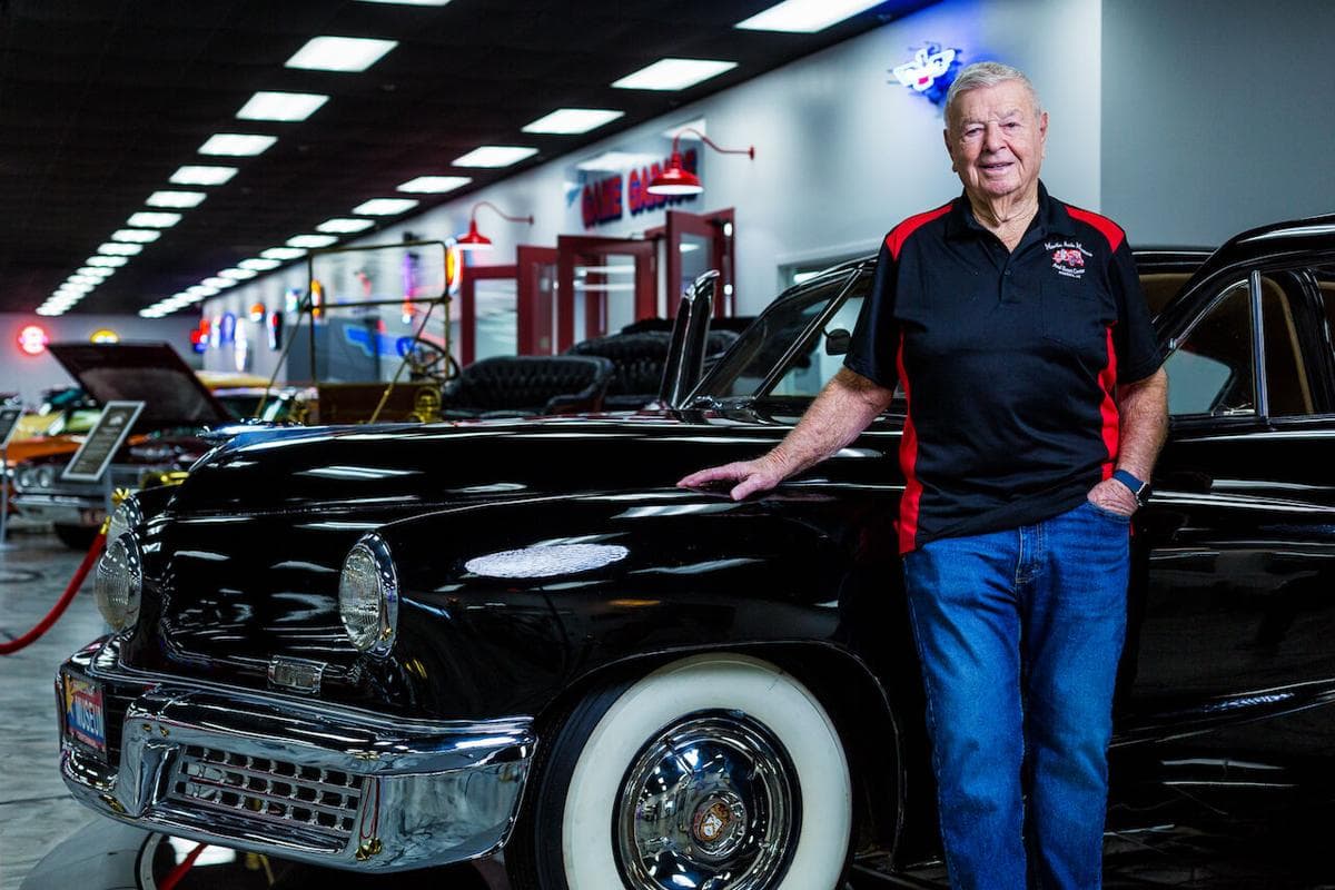 Museum founder Mel Martin standing beside a black classic car on the museum floor