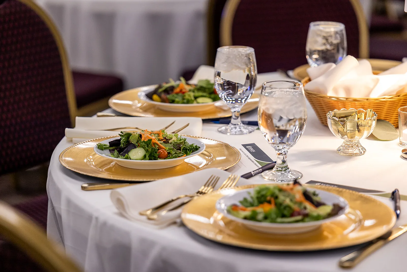 A plated salad course with bread and water at each seat