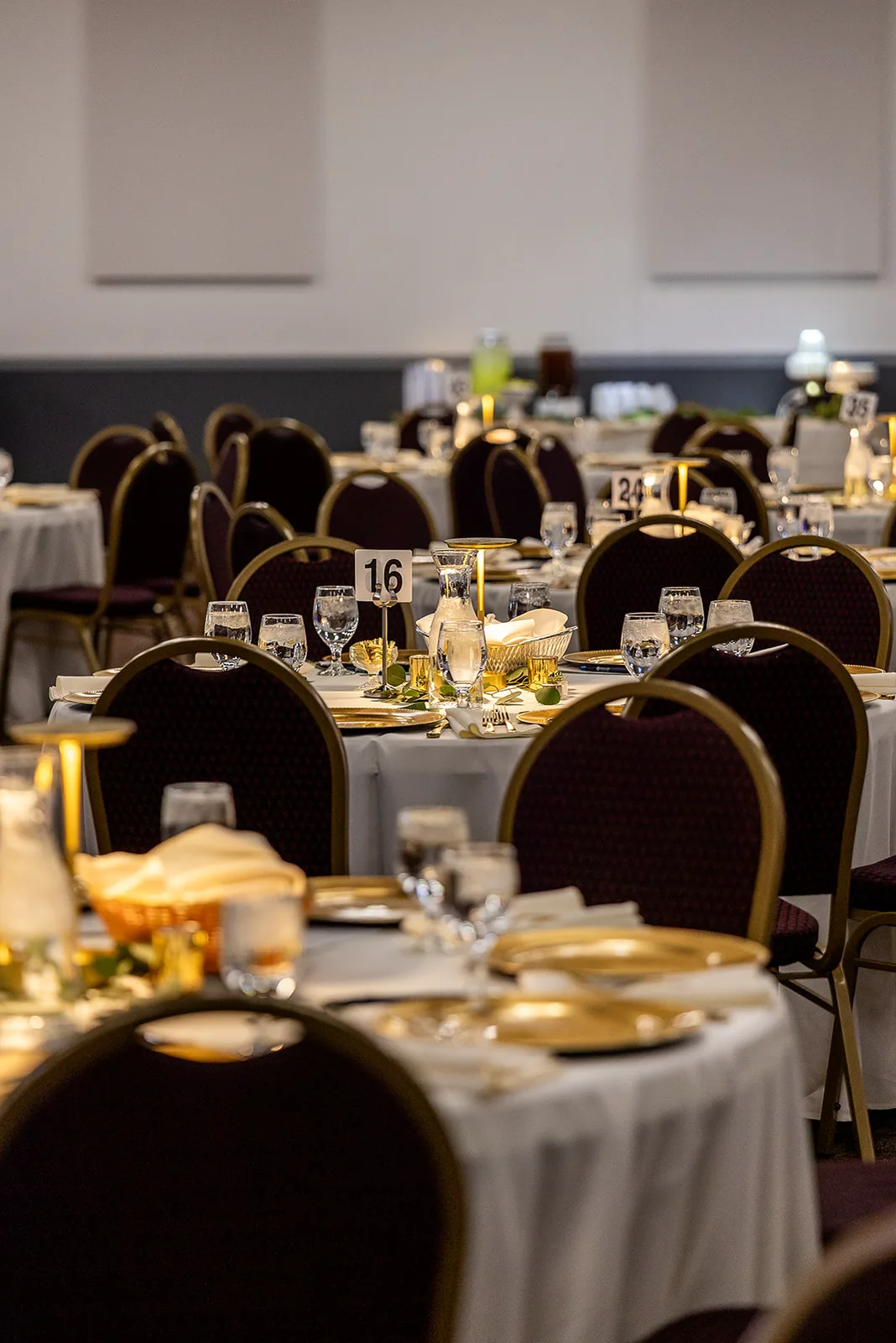 A round table dressed in white linen with gold chargers and candlelight